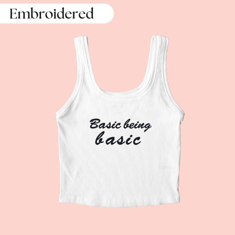 Pu&ograve; includere: Canotta bianca con il testo "Basic being basic" ricamato in nero.