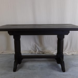 May include: A rectangular wooden table with a dark brown finish, featuring a smooth flat top surface supported by two thick, turned pedestal legs connected by a horizontal stretcher bar near the base, providing a sturdy and stable foundation.