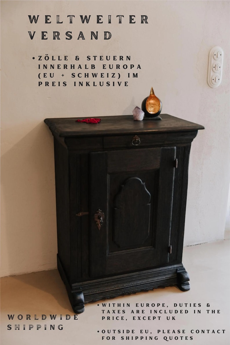 May include: A dark stained wooden cabinet with a single door and a small drawer. The cabinet has decorative molding and a metal handle. A small, gold-colored object sits on top, along with a crystal and a red object.