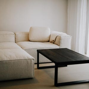 Puede incluir: Un sofá seccional blanco con una mesa de café de madera oscura en una sala de estar moderna.