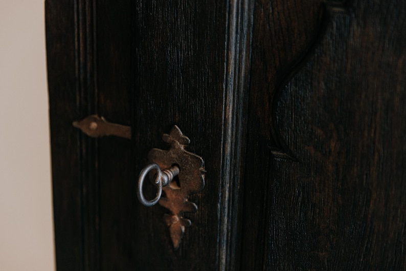 May include: Close-up of a dark wooden door with a vintage, ornate keyhole and key. The keyhole and key are made of aged, rusty metal. The door's wood grain is visible, with vertical lines and a dark brown color.