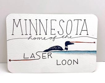 Könnte beinhalten: Eine weiße Karte mit schwarzem handschriftlichem Text, der "Minnesota, home of the laser loon" lautet. Auf der Karte ist ein Cartoon-Luchs mit einem roten Laserstrahl aus seinen Augen abgebildet.