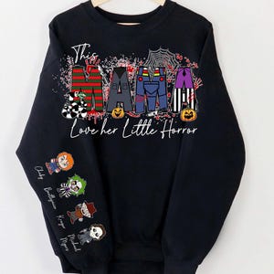 May include: Black sweatshirt with the text "This Mama Loves her Little Horror." The word "MAMA" is designed with horror movie character themes. The sleeve features cartoon characters. A Halloween-themed apparel item.