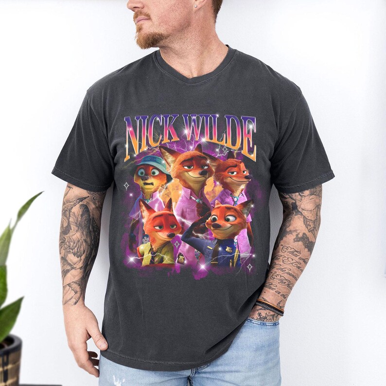 Puede incluir: Camiseta gris oscuro con un dise&ntilde;o de Nick Wilde de Zootr&oacute;polis. El dise&ntilde;o incluye m&uacute;ltiples im&aacute;genes del personaje con el texto "NICK WILDE" en un estilo retro. La camiseta tiene cuello redondo y mangas cortas.