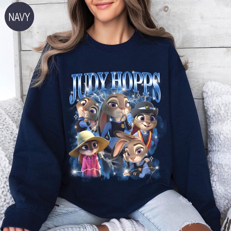 Puede incluir: Sudadera azul marino con un dise&ntilde;o de Judy Hopps y otros personajes de Zootopia. El dise&ntilde;o incluye el texto "JUDY HOPPS" en una fuente estilizada, con acentos de rayos. La sudadera es de cuello redondo.