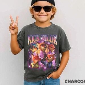 Puede incluir: Camiseta gris carb&oacute;n con un gr&aacute;fico de Nick Wilde de Zootopia. El dise&ntilde;o incluye el texto "NICK WILDE" en un estilo retro, con im&aacute;genes del personaje. La camiseta es de estilo vintage.