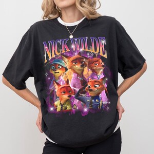 Puede incluir: Camiseta negra con un dise&ntilde;o de Nick Wilde y otros personajes de Zootopia. El dise&ntilde;o incluye el texto "NICK WILDE" en un estilo retro con acentos morados y amarillos. La camiseta tiene cuello redondo y mangas cortas.