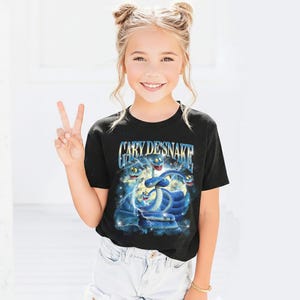 Puede incluir: Camiseta negra con el texto "Gary DeSnake" y un gr&aacute;fico de serpientes azules de dibujos animados. Las serpientes est&aacute;n sobre un fondo estrellado. La camiseta la lleva una persona.