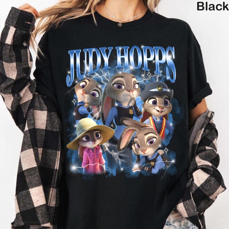 Puede incluir: Camiseta negra con un dise&ntilde;o de Judy Hopps de Zootr&oacute;polis. El dise&ntilde;o incluye el texto "JUDY HOPPS" en azul, junto con ilustraciones de Judy en varias poses, rodeadas de rayos.