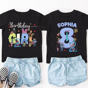 K&ouml;nnte beinhalten: Zwei schwarze T-Shirts mit bunten Grafiken und Text. Eines zeigt "Birthday Girl" mit Zeichentrickfiguren. Das andere zeigt "Sophia 8" mit Zeichentrickfiguren. Kombiniert mit hellblauen Jeansshorts und karierten Slip-On-Schuhen.