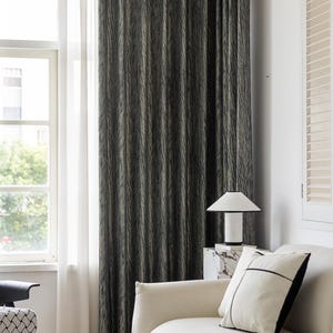 May include: Dark gray and beige patterned curtain hanging in front of a window. The curtain has vertical lines and is next to a sheer white curtain. A white lamp sits on a marble table next to a white sofa with a black and white pillow.