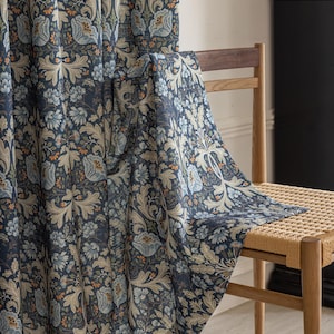 May include: Dark blue floral patterned curtain fabric draped over a wooden chair. The fabric features a repeating design of stylized flowers and leaves in shades of blue, beige, and orange. The chair has a woven seat.