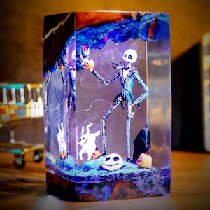 May include: A clear resin block featuring a skeletal figure in a pinstripe suit, holding a pumpkin. The scene includes other Halloween-themed characters, pumpkins, and a spooky backdrop. The artwork is a unique decorative piece.