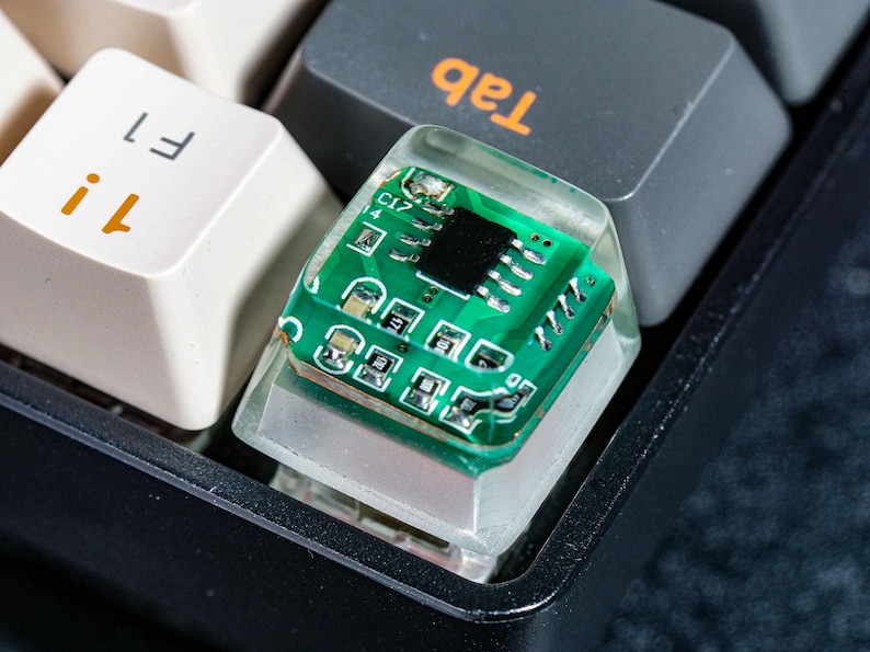 May include: A clear keycap with a green circuit board inside. The keycap is labeled "Tab" and is on a black keyboard.