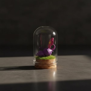 May include: A miniature purple creature with a pink flower is displayed inside a glass dome. The creature rests on a bed of green grass atop a cork base. The dome sits on a gray surface.