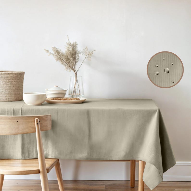 Puede incluir: Un mantel de mesa beige claro con una textura sutil, mostrado sobre una mesa de madera con una silla de madera. Un jarr&oacute;n con flores secas y un cuenco de platos est&aacute;n sobre la mesa. Un primer plano del mantel muestra gotas de agua perlando en la superficie.