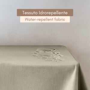 Puede incluir: Primer plano de un mantel beige claro con gotas de agua en la superficie. El texto "Tessuto Idroreppellente Water-repellent fabric" se muestra sobre el mantel.