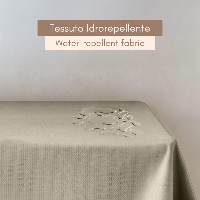 Puede incluir: Primer plano de un mantel beige claro con gotas de agua en la superficie. El texto "Tessuto Idroreppellente Water-repellent fabric" se muestra sobre el mantel.