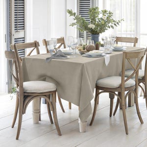 Puede incluir: Un mantel de lino beige con textura natural est&aacute; colocado sobre una mesa de madera. La mesa est&aacute; puesta con seis sillas, vasos y un centro de mesa con vegetaci&oacute;n.
