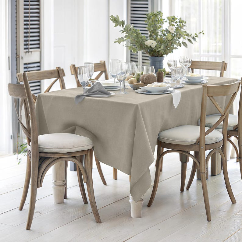 Puede incluir: Un mantel de lino beige con textura natural est&aacute; colocado sobre una mesa de madera. La mesa est&aacute; puesta con seis sillas, vasos y un centro de mesa con vegetaci&oacute;n.