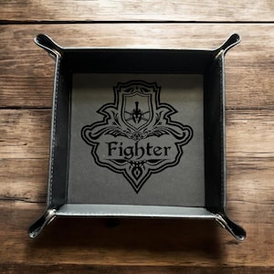 May include: A square, gray and black dice tray with a decorative Fighter emblem. The tray has a black border and rounded corners. The emblem features a shield, spear, and the word "Fighter" in a stylized font.