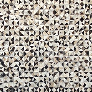 Könnte beinhalten: Ein geometrischer Musterteppich aus Kuhfell. Der Teppich besteht aus kleinen Dreiecken in den Farben Schwarz, Weiß und Braun.
