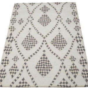 Pode incluir: Um tapete branco com um padrão geométrico de diamantes pretos e cinzentos. O tapete tem um brilho subtil e uma textura macia.