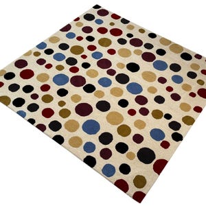 May include: A cream-colored rug with a repeating pattern of colorful polka dots. The dots are in shades of red, blue, black, brown, and gold.