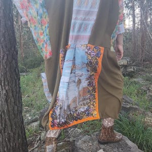 Può includere: Un lungo kimono verde, marrone e blu con motivo floreale. Il kimono è indossato da una persona in piedi su uno scoglio.