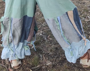 Op de afbeelding: Een patchwork broek in groen, blauw en bruin. De broek heeft een wijd been ontwerp met decoratieve linten en een geschulpte zoom. De stof lijkt een zacht, vloeiend materiaal te zijn.