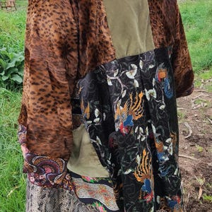 Könnte beinhalten: Ein braunes, grünes und schwarzes Patchwork-Kimono mit einem floralen und Vogel-Druck. Das Kimono hat eine lange, fließende Silhouette und ist aus verschiedenen Stoffen gefertigt.