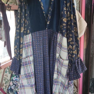 Pode incluir: Um vestido comprido de manga comprida com decote em V. O vestido é feito de diferentes tecidos, incluindo veludo preto, estampa de leopardo marrom e dourado e tecido xadrez. O vestido tem um caimento solto e uma saia fluida.
