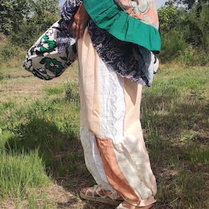 Può includere: Una giacca verde con cappuccio e maniche voluminose con motivi paisley color pesca, blu e bianco, abbinata a pantaloni patchwork in tonalità pesca e pizzo bianco. L'outfit è completato da sandali bianchi con fiori colorati lavorati all'uncinetto.