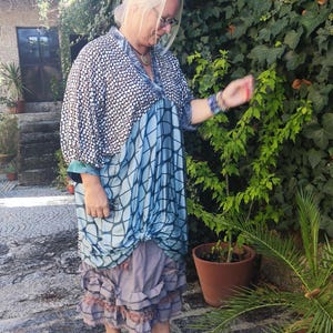 Puede incluir: Un vestido hasta la rodilla con un corpiño de patrón blanco y negro con escote en V, una sección de falda con patrón de cuadrícula azul y negro con un detalle de nudo frontal y un dobladillo gris con volantes, junto con zuecos azules.