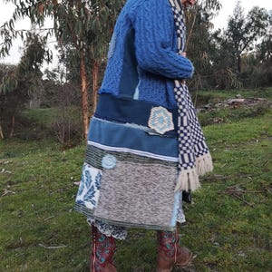 May include: A long-sleeved blue cable-knit cardigan featuring a patchwork design with various blue and grey fabric panels, a white and blue checkered scarf with fringe, and brown leather boots with red and blue decorative stitching.