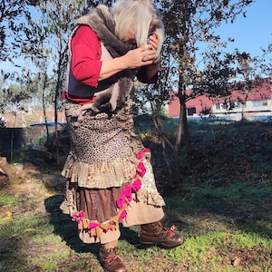 Peut inclure: Une personne porte un haut rouge, un gilet et une écharpe en fausse fourrure. La tenue comprend une jupe à volants avec un imprimé léopard, des volants marron et beige, et des accents roses. Des bottes marron complètent le look.