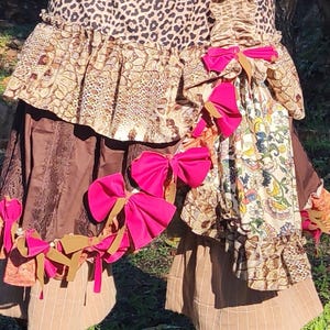 Può includere: Un outfit multistrato con un top con stampa leopardata, gonne marroni e fiocchi decorativi. L'ensemble include una gonna fantasia con accenti floreali e animalier e stivali marroni con fiocchi.