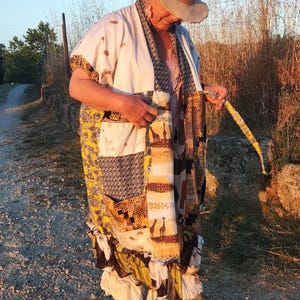 Puede incluir: Una bata estilo kimono de patchwork con una mezcla de estampados animales, siluetas de jirafas y patrones geométricos en tonos amarillos, marrones y blancos. La prenda tiene un cuello ancho, mangas cortas y un dobladillo con volantes.