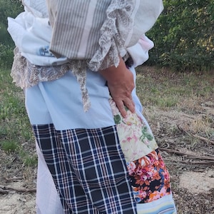 Puede incluir: Una prenda de patchwork que presenta una variedad de patrones de tela, incluyendo cuadros negros y blancos, paneles sólidos azul claro y estampados florales con acentos rosas y verdes. La pieza incorpora detalles de volantes y secciones a rayas.