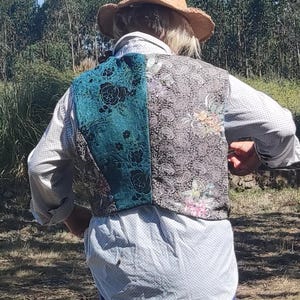 Peut inclure: Un gilet patchwork avec un panneau floral turquoise et un panneau cachemire avec des accents floraux. Le gilet est porté sur une chemise blanche et une jupe bleue. Un chapeau de paille est porté.