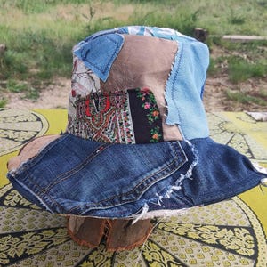 Puede incluir: Un sombrero de cubo patchwork con ala y corona de mezclilla. El sombrero presenta varios parches de tela en tonos de azul, marrón y textiles estampados. El ala está hecha de mezclilla reciclada, y la corona tiene una mezcla de telas.
