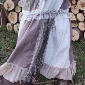 Può includere: Una gonna patchwork con un design a strati. La gonna presenta vari tessuti nei toni del marrone, bianco e grigio, con sezioni a righe e fantasia. Volant e bordi in pizzo rifiniscono l'orlo. Gli stivali in pelle marrone sono visibili in basso.