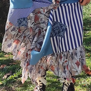 Op de afbeelding: Een patchwork rok met blauwe, witte en bloemenpatronen. De rok heeft een mix van strepen, effen kleuren en bloemenprints. Bruine leren laarzen met witte veters maken de look compleet. De rok is gelaagd en heeft een geplooid zoom.