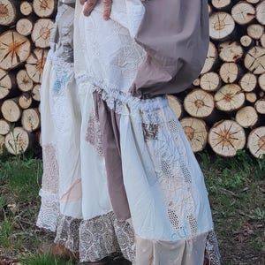 Può includere: Una gonna a strati dall'estetica bohémien. La gonna presenta pannelli bianchi, marrone chiaro e fantasia, rifiniti con pizzo e balze. Stivali marroni completano il look rustico e vintage.