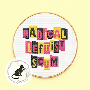 以下が含まれることがあります： 「RADICAL LEFTIST SCUM」の文字が黒、ピンク、黄色で刺繍されたクロスステッチの刺繍枠。デザインは白い生地にあり、金色のフープで囲まれています。左下隅には黒猫の小さなロゴがあります。
