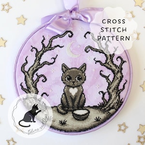 May include: A round embroidery hoop containing a cross stitch pattern of a grey cat with a white heart on its chest, sitting between two dark, leafless trees under a crescent moon against a light purple background, topped with a lavender ribbon.