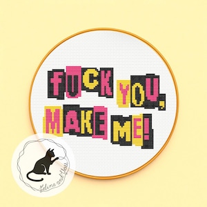 May include: Cross-stitch embroidery in a wooden hoop. The text "FUCK YOU. MAKE ME!" is stitched in black, pink, and yellow. A small logo of a black cat is in the lower left corner.