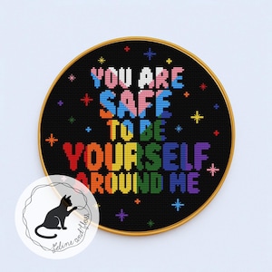 Peut inclure: Broderie au point de croix circulaire dans un cerceau en bois. Le tissu noir porte l'inscription "YOU ARE SAFE TO BE YOURSELF AROUND ME" aux couleurs de l'arc-en-ciel. Étoiles décoratives et logo de chat noir.