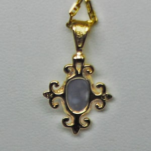 May include: A gold-colored pendant necklace with an ornate, cross-shaped design. The pendant features a central, oval-shaped, light-blue stone. The necklace chain is also gold-colored.