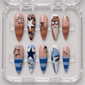May include: A set of ten almond-shaped press-on nails in a clear plastic case. The top row features brown stripes, a white star, and a cartoon character illustration. The bottom row features blue stripes, a dark blue star, and a blue character.
